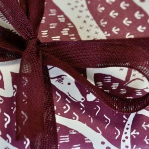 A parcel wrapped with Wine ribbon and Dogs Blackcurrant Squash paper by Cambridge Imprint